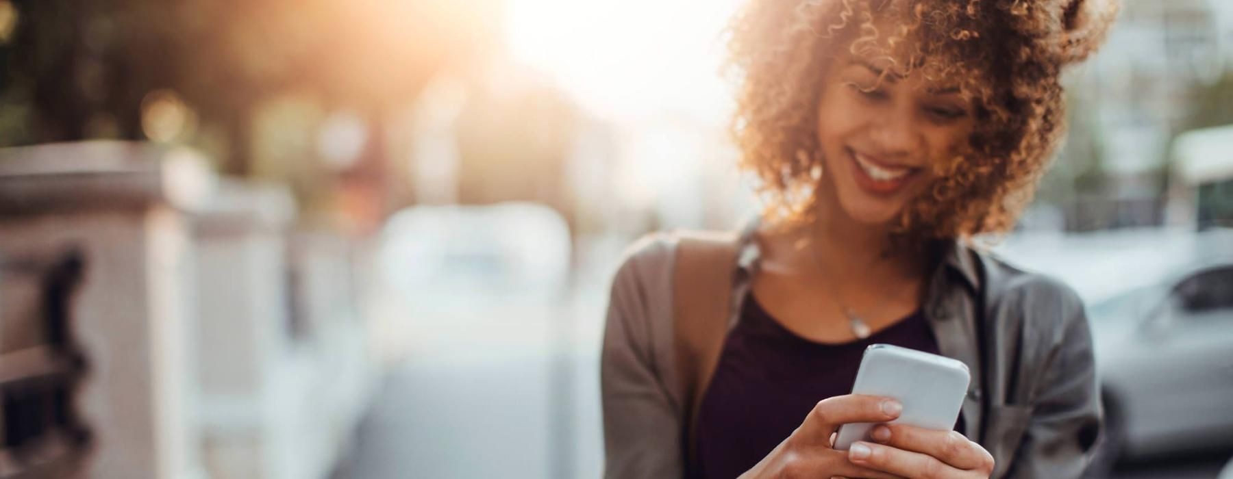 woman texts on her phone as she walks through the city