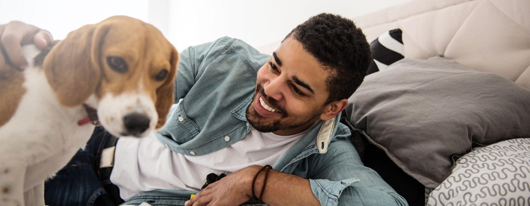 man smiles and pets his dog on a bed